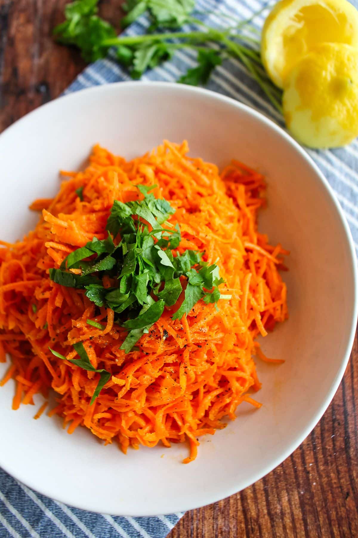 Middle eastern carrot salad garnished with fresh herbs on a wooden background with a towel.