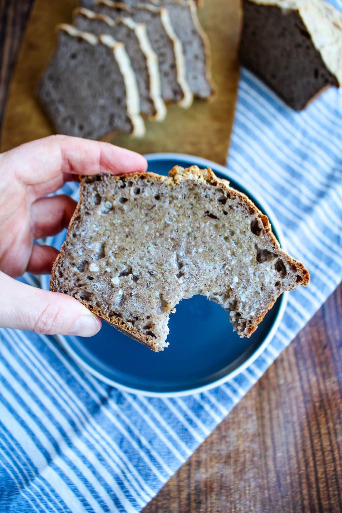 A hand holding up a slice of buckwheat bread with a bite missing.