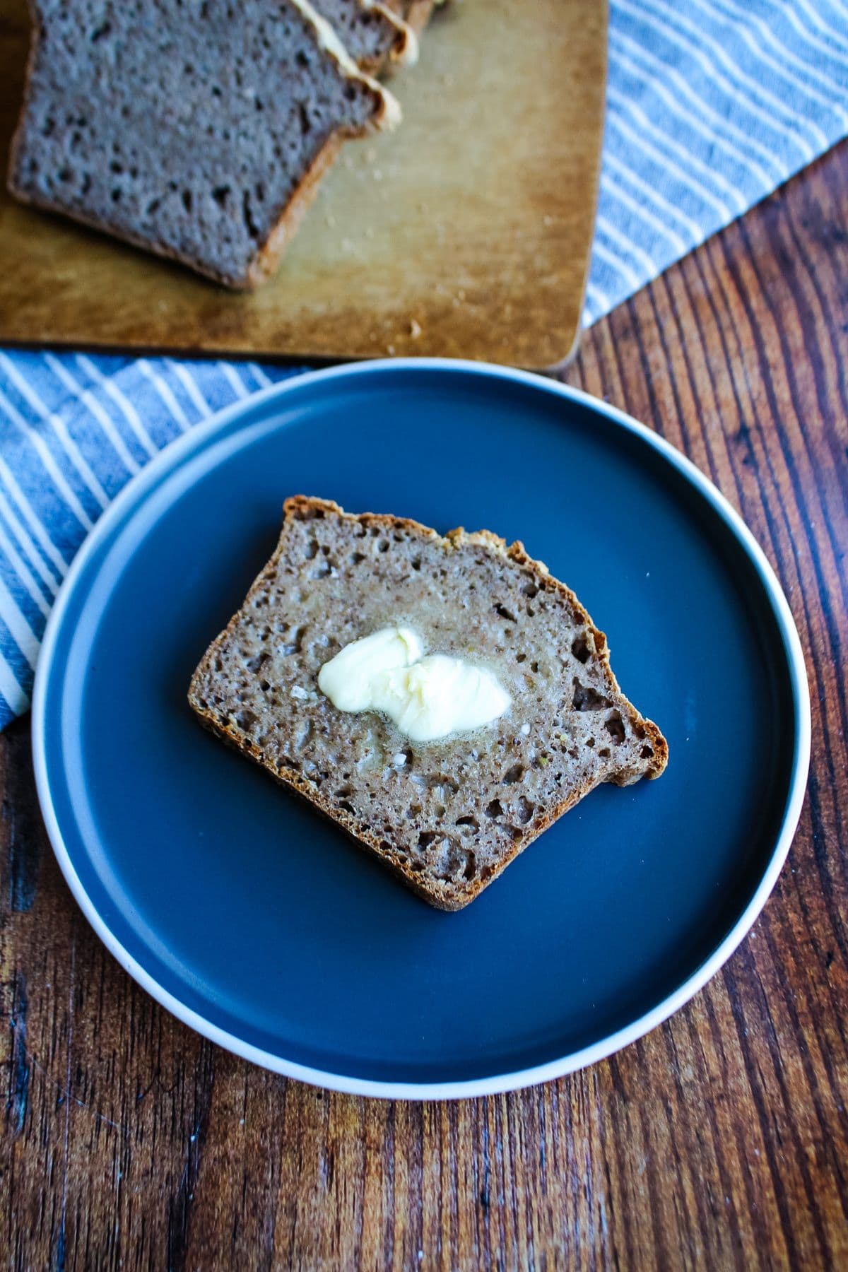 Slice of gluten free bread on a plate topped with butter.
