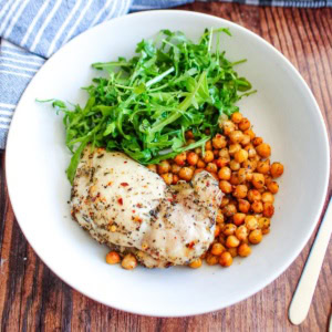 Crispy oven baked chicken and chickpeas on a white plate with a side of arugula salad.