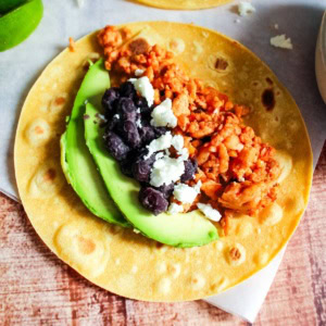 A ground chicken taco topped with black beans, avocado, and crumbled white cheese.