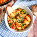 A bowl of marry me butter beans with a piece of bread dipping in.