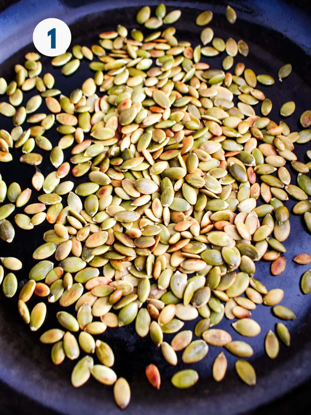 Pumpkin seeds added to a skillet.
