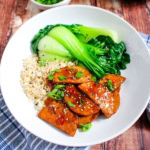 Teriyaki tempeh on a white plate with some brown rice and bok choy.