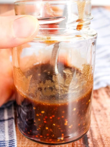 A jar of mustard balsamic dressing held by a hand over the table.