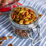A jar of roasted pumpkin seeds on the table with a few scattered on the table.