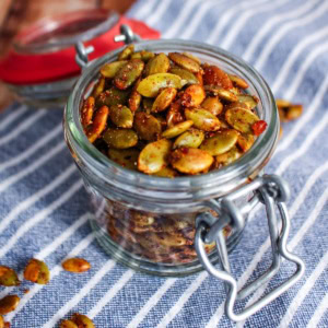 A jar of roasted pumpkin seeds on the table with a few scattered on the table.