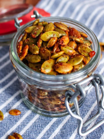 A jar of roasted pumpkin seeds on the table with a few scattered on the table.