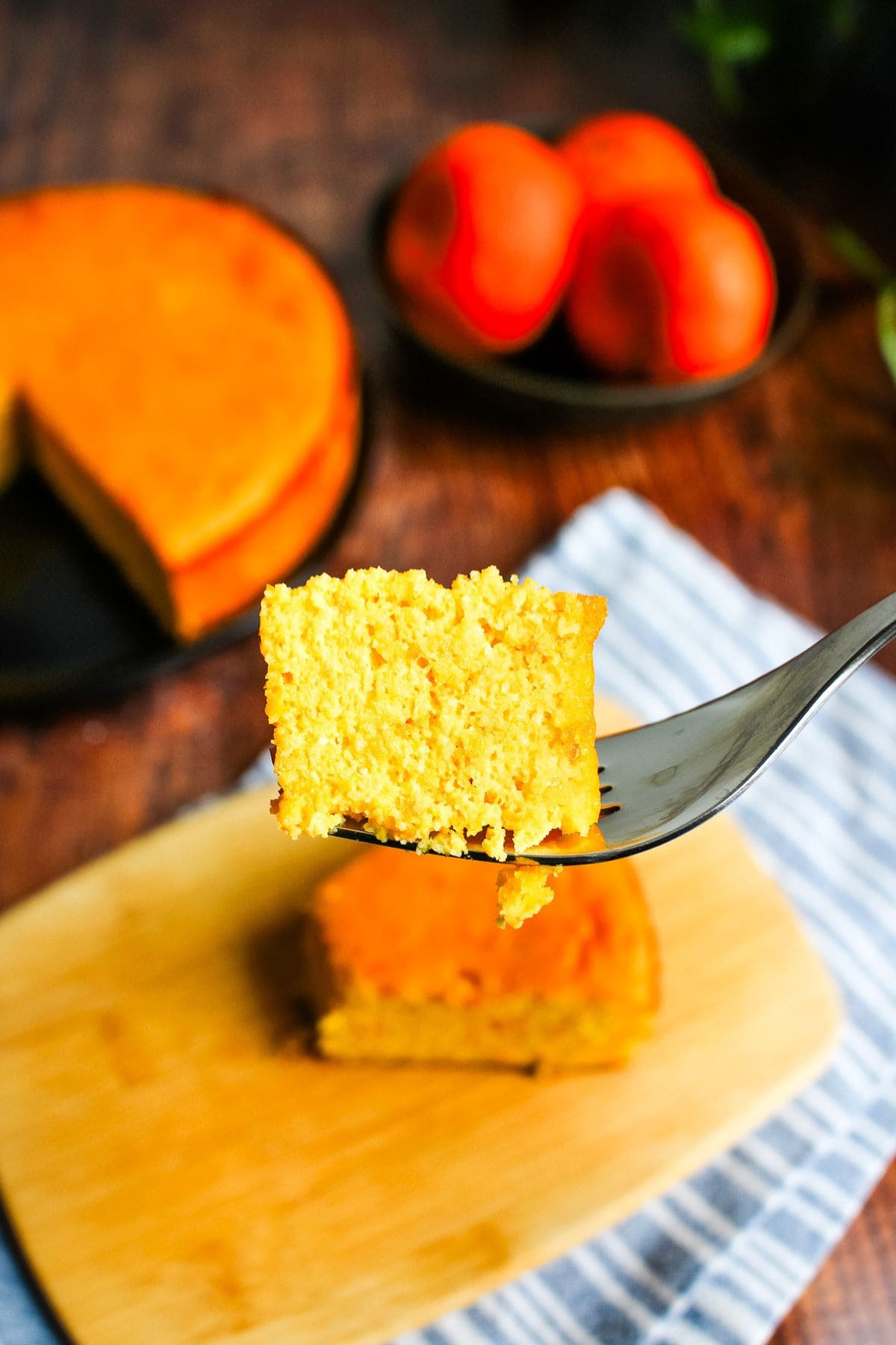 A bite of clementine cake held up over the slice of cake on the table.