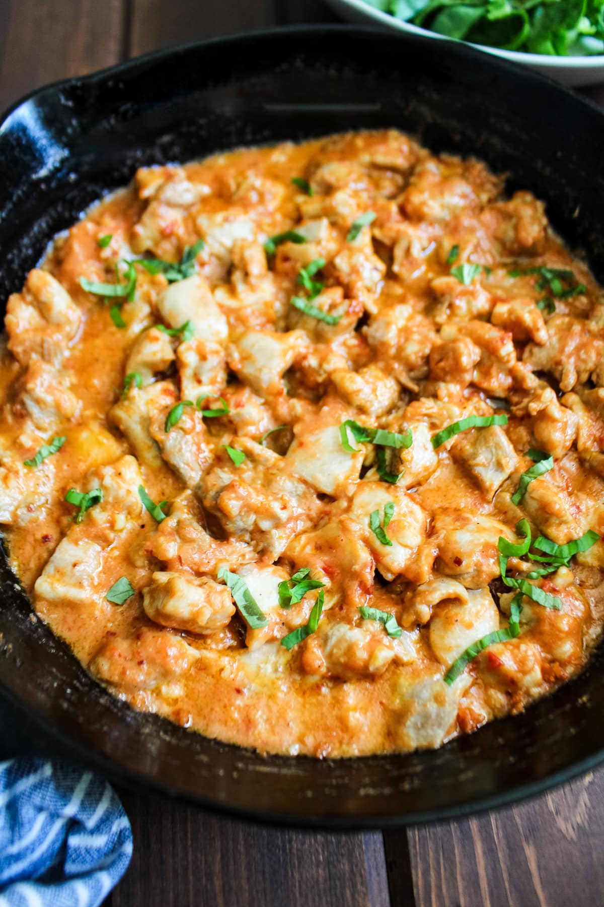 Chicken cooked in cottage cheese sauce with tomatoes in a skillet garnished with basil.