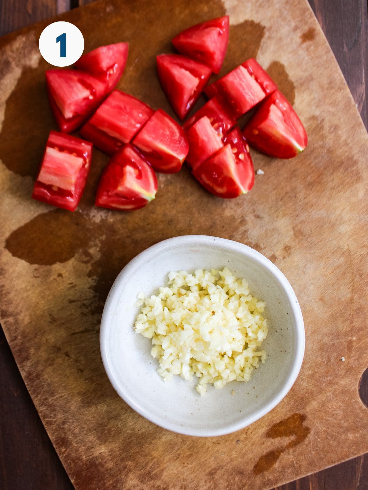Minced garlic and diced tomato on a cutting board.