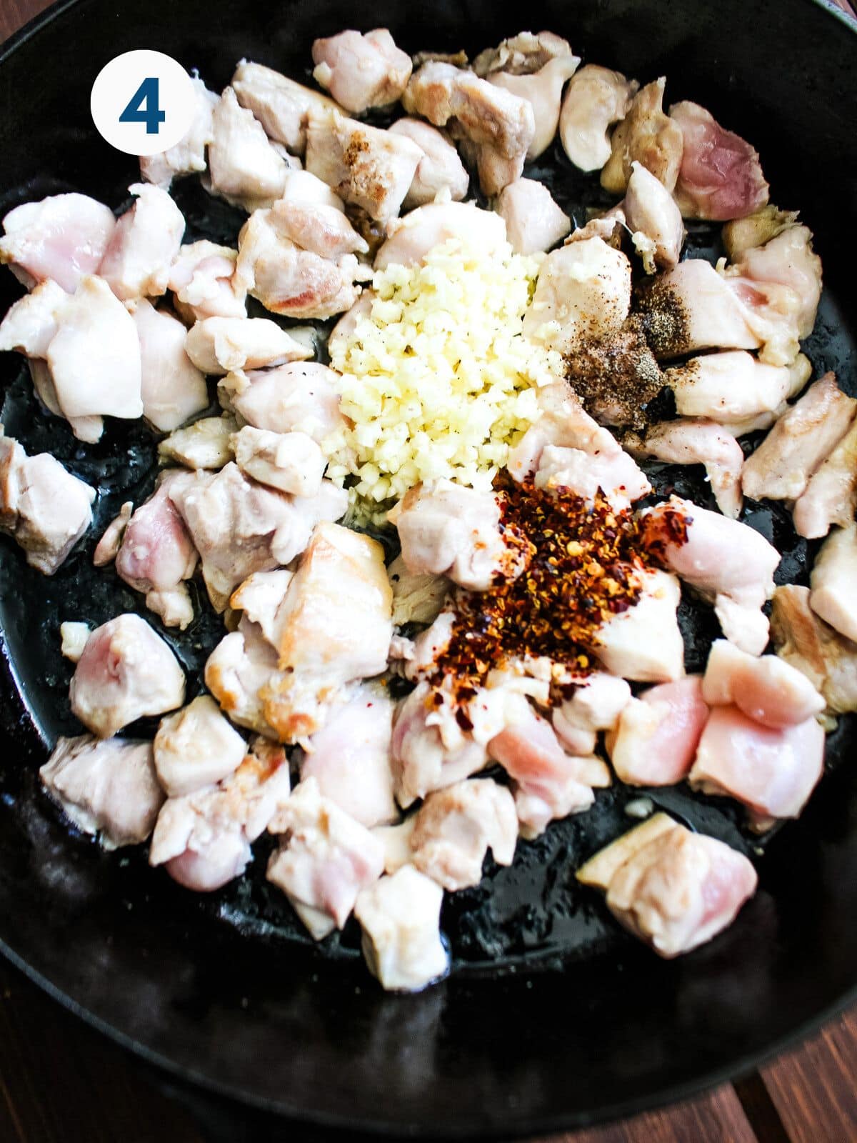 Minced garlic and seasonings added to the chicken cooking in a skillet.