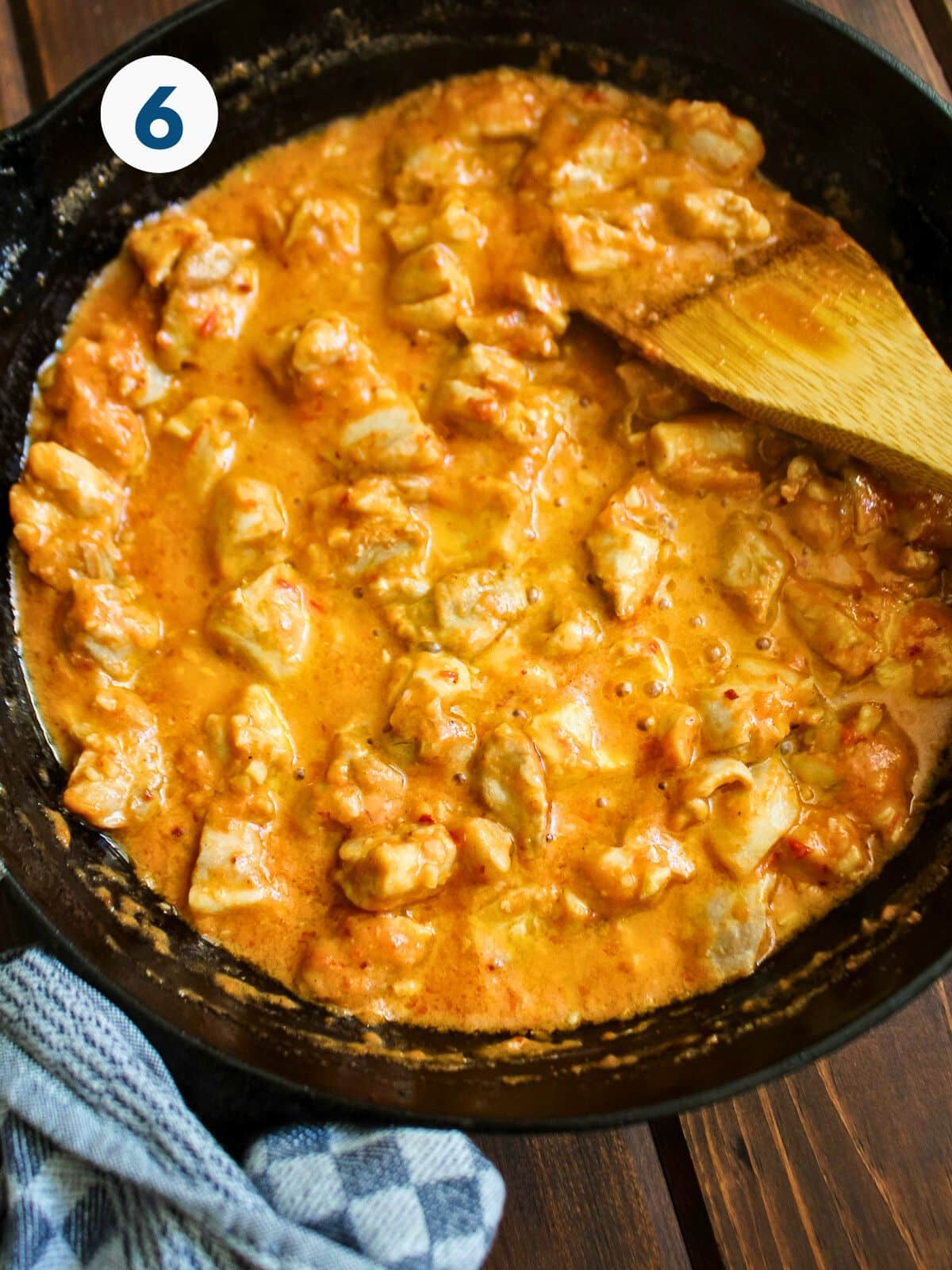 Chicken in pink cottage cheese sauce stirred with a wooden spatula.